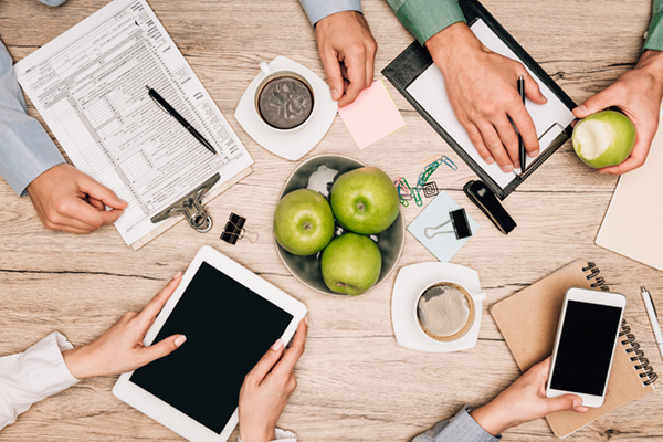many people reviewing documents surrounding a bowl of apples